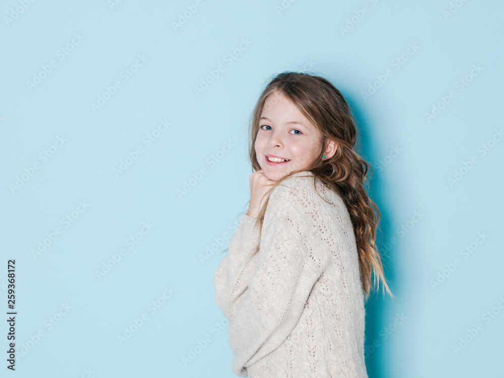 pretty and cool 9 year old girl with brown wool sweater posing in front of blue background pretty and cool 9 year old girl with brown wool sweater posing in front of blue background