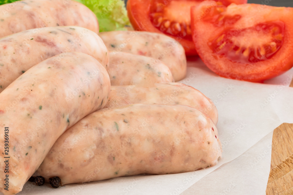 Fresh raw sausage with lettuce and tomato on the wooden background Fresh raw sausage with lettuce and tomato on the wooden background