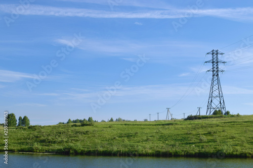Landscape with row of electric poles over wild river across meadow with clear sky