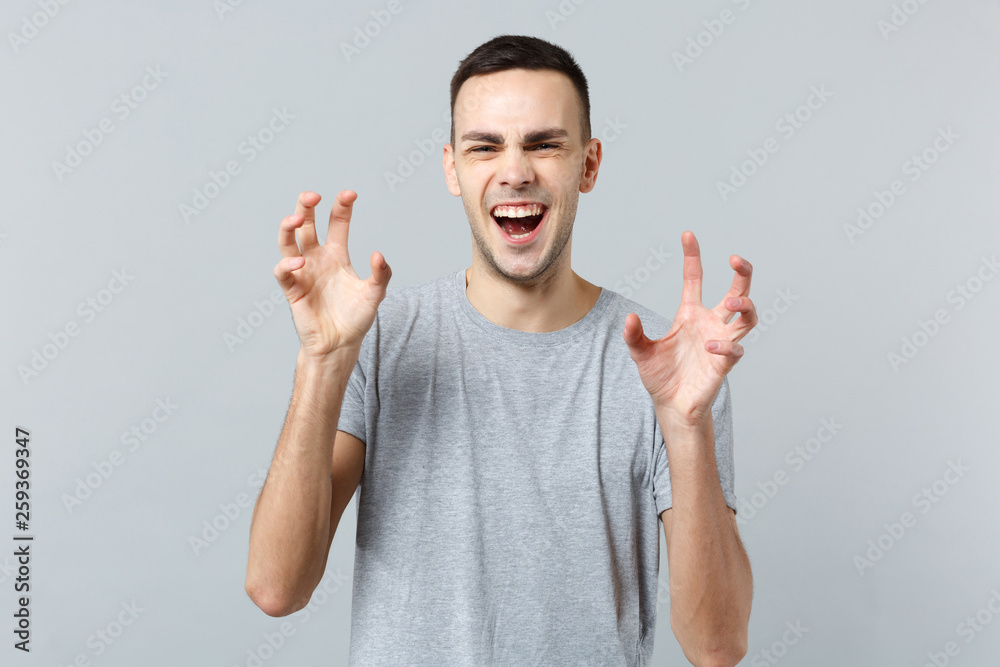 Portrait of funny young man in casual clothes shouting, growling like animal, making cat claws gesture isolated on grey wall background. People sincere emotions, lifestyle concept. Mock up copy space. Portrait of funny young man in casual clothes shouting, growling like animal, making cat claws gesture isolated on grey wall background. People sincere emotions, lifestyle concept. Mock up copy space.