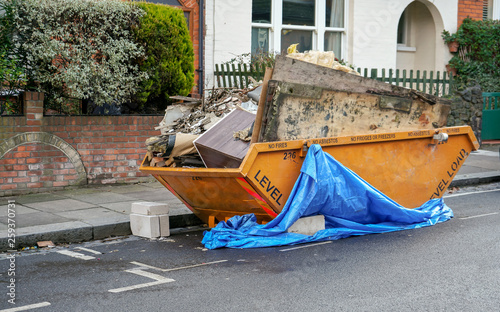 Large orange metal skip container in front house, full of rubbish from household reconstruction photo
