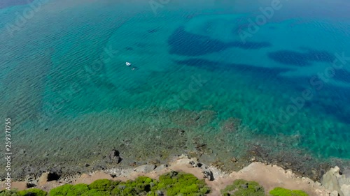 Aerial view of blue sea surface on rocky coast with light reflections. Top view of transparent turquoise ocean water surface and rocks on shore.