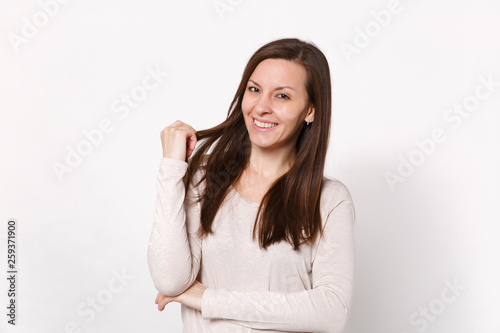 Portrait of attractive smiling young woman in light clothes looking camera, holding hair isolated on white wall background in studio. People sincere emotions, lifestyle concept. Mock up copy space.