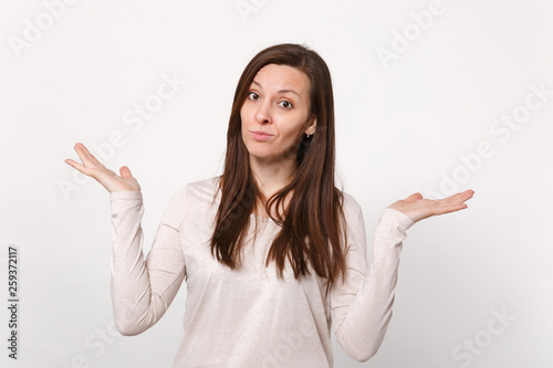 Portrait of puzzled concerned young woman in light clothes spreading and pointing hands aside isolated on white background in studio. People sincere emotions, lifestyle concept. Mock up copy space.