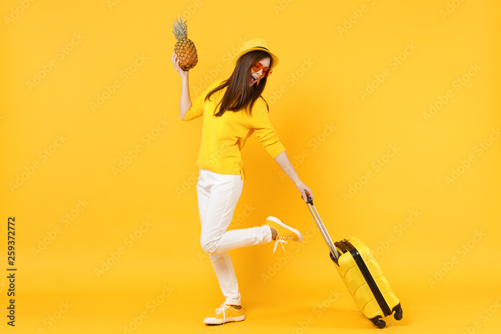 Pretty traveler tourist woman in summer clothes, hat hold fresh ripe pineapple fruit isolated on yellow orange background. Passenger traveling abroad on weekends getaway. Air flight journey concept. Pretty traveler tourist woman in summer clothes, hat hold fresh ripe pineapple fruit isolated on yellow orange background. Passenger traveling abroad on weekends getaway. Air flight journey concept.