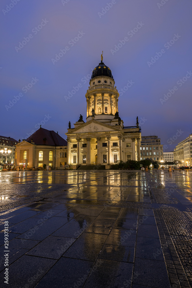 Illuminated Französischer Dom (French Cathedral) and its reflection at the wet Gendarmenmarkt Square in Berlin, Germany, in the evening.