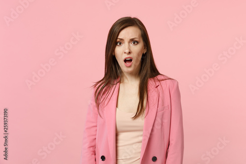 Portrait of shocked concerned irritated young woman wearing jacket keeping mouth open isolated on pastel pink wall background in studio. People sincere emotions, lifestyle concept. Mock up copy space. © ViDi Studio