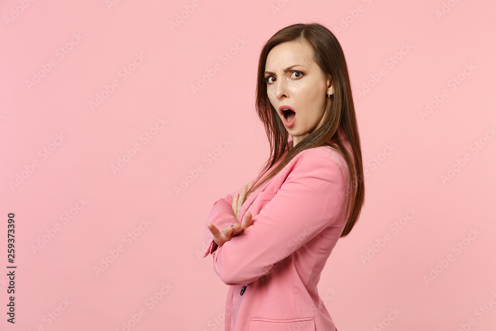 Side view of perplexed irritated young woman wearing jacket keeping mouth open, holding hands crossed isolated on pastel pink background. People sincere emotions lifestyle concept. Mock up copy space. Side view of perplexed irritated young woman wearing jacket keeping mouth open, holding hands crossed isolated on pastel pink background. People sincere emotions lifestyle concept. Mock up copy space.