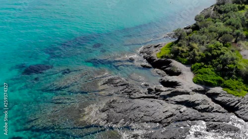 Aerial view of blue sea surface on rocky coast with light reflections. Top view of transparent turquoise ocean water surface and rocks on shore.