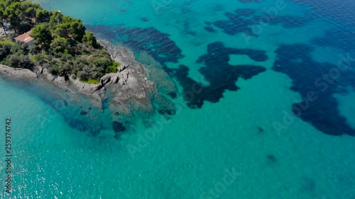 Aerial view of blue sea surface on rocky coast with light reflections. Top view of transparent turquoise ocean water surface and rocks on shore.
