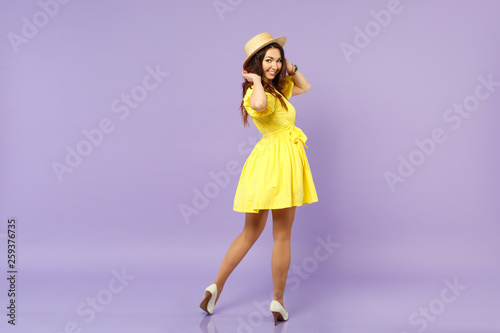Back rear view of smiling young woman in yellow dress, summer hat looking back, rising hands isolated on pastel violet wall background. People sincere emotions, lifestyle concept. Mock up copy space.