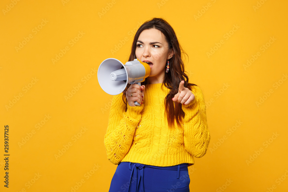 Puzzled young woman in sweater, blue trousers pointing index finger on camera, scream in megaphone isolated on yellow orange background. People sincere emotions, lifestyle concept. Mock up copy space. Puzzled young woman in sweater, blue trousers pointing index finger on camera, scream in megaphone isolated on yellow orange background. People sincere emotions, lifestyle concept. Mock up copy space.