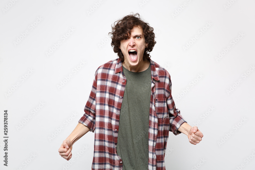 Portrait of angry irritated screaming young man in casual clothes looking camera clenching fists isolated on white background in studio. People sincere emotions, lifestyle concept. Mock up copy space. Portrait of angry irritated screaming young man in casual clothes looking camera clenching fists isolated on white background in studio. People sincere emotions, lifestyle concept. Mock up copy space.