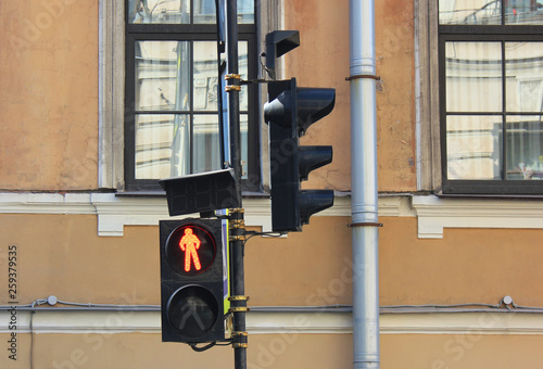 Red traffic light on city street in front of old building facade. Stop signal showing a standing man figure on classic black traffic light at pedestrian crosswalk in downtown street