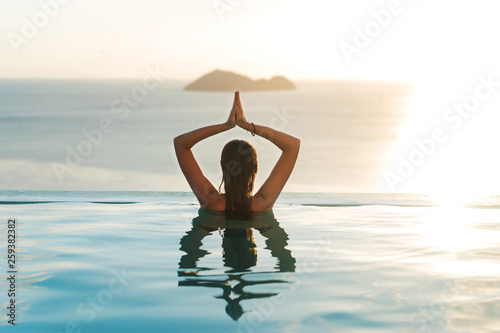 girl in the pool at sunset doing yoga with a view of the mountains and the sea