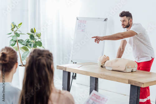 handsome instructor with cpr dummy pointing with finger during first aid training class photo