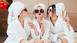 Celebration party at spa. Friends congratulation. Young women with champagne. Sunglasses, bathrobes and turbans on.