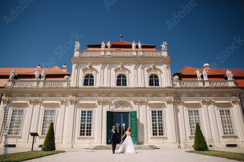 Beautiful young bride with her handsome groom walking in palace Belvedere