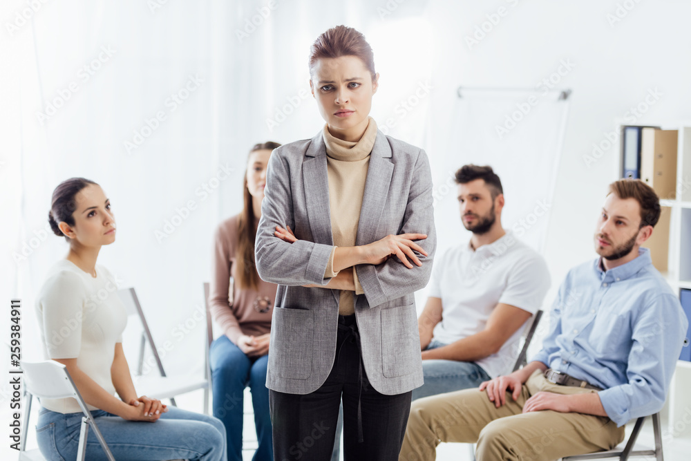 woman looking at camera while people sitting on chairs during group therapy session woman looking at camera while people sitting on chairs during group therapy session