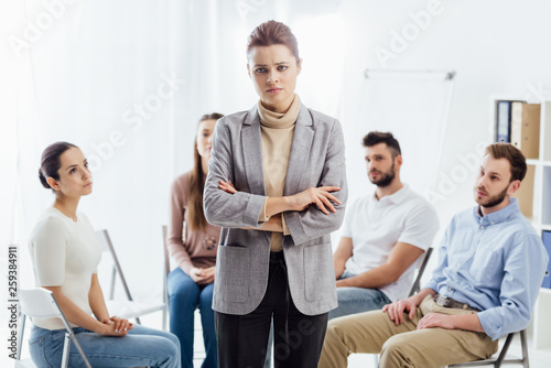 woman looking at camera while people sitting on chairs during group therapy session