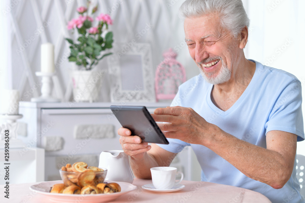 senior man using tablet while drinking tea senior man using tablet while drinking tea