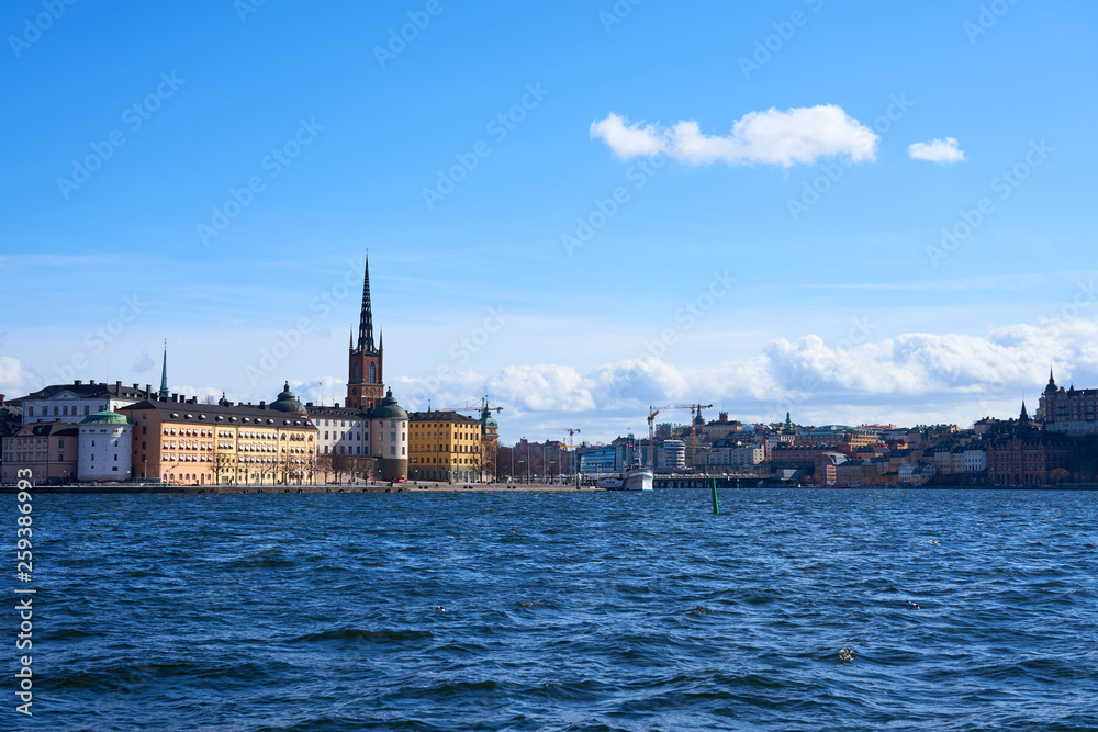 Old city of Stockholm with waves on blue water under the blue cloudy sky in sunshine.