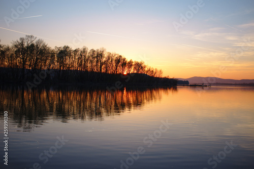 Sunset in strong colors over a river with reflections of trees