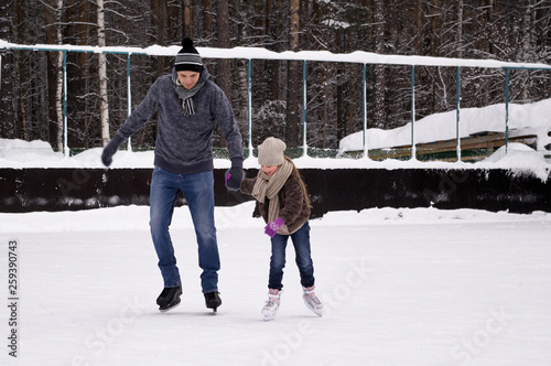 Daddy and daughter skate on the rink under the open sky on a winter day