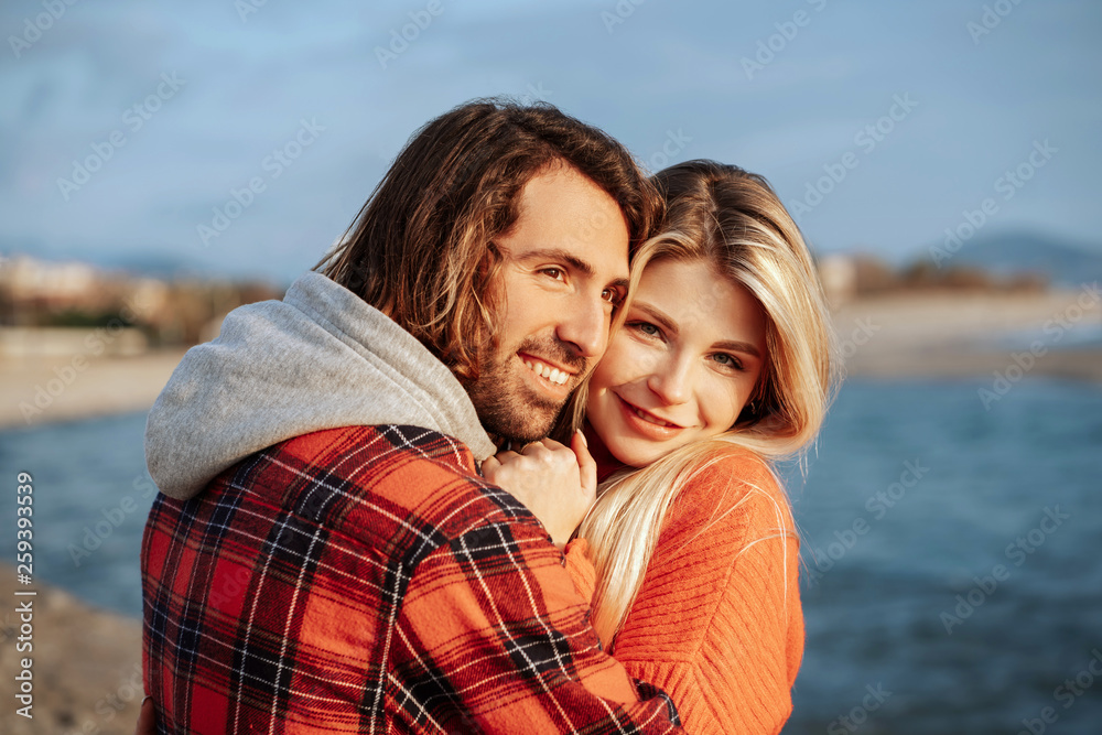 Young couple on beach hugging and looking at sunset. Holidays at sea on vacation. Close up portrait. Young couple on beach hugging and looking at sunset. Holidays at sea on vacation. Close up portrait.