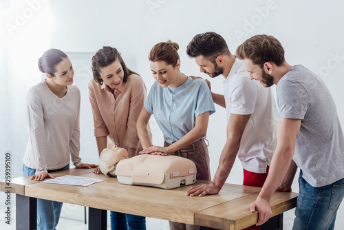 group of smiling people performing cpr on dummy during first aid training photo