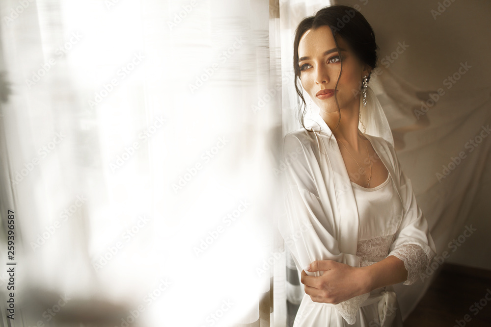 Bride in beautiful dress sitting on chair indoors in white studio interior like at home. Trendy wedding style shot. Bride in beautiful dress sitting on chair indoors in white studio interior like at home. Trendy wedding style shot.