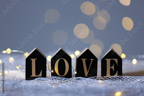 Word LOVE of wooden letters on mesh fabric against blurred lights. Bokeh effect