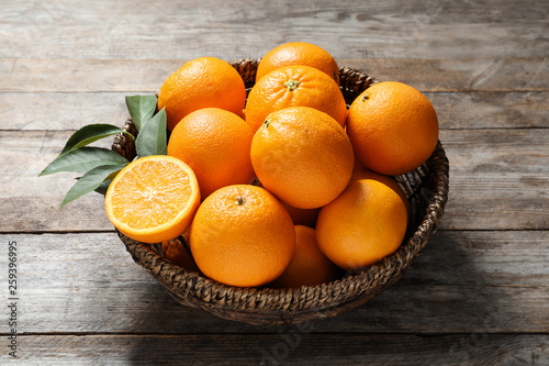 Wicker bowl with ripe oranges on wooden background