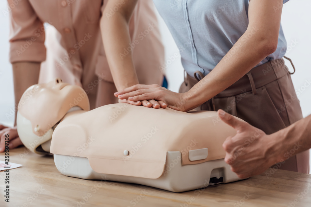 cropped view of woman performing chest compression on dummy during cpr training class while man doing thumb up sign