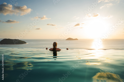 Fototapeta Naklejka Na Ścianę i Meble -  girl in the pool at sunset with views of the mountains and the sea