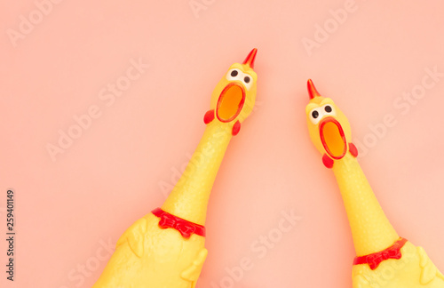 Two screaming chicken toys are isolated on a pastel coral background, screaming with a mouth open looking into the camera. Chicken toy on a pink background, pattern for design.