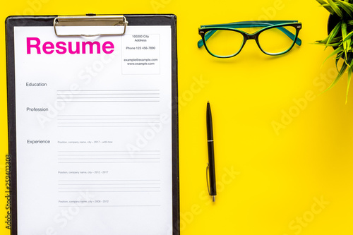 Empoyment concept with resume on yellow work desk background with pen, glasses top view photo