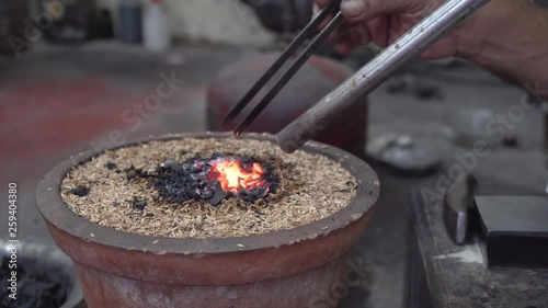 Close up on traditional ethnic master gold smith using hammer to work creative jewellery in workshop, India. photo