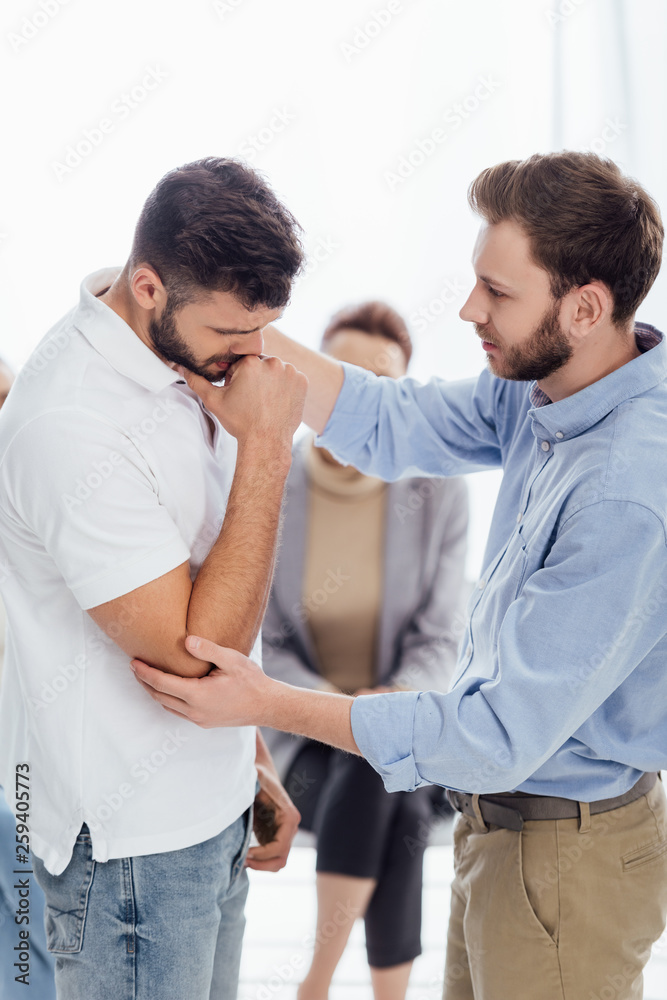 selective focus of man consoling upset man during therapy meeting