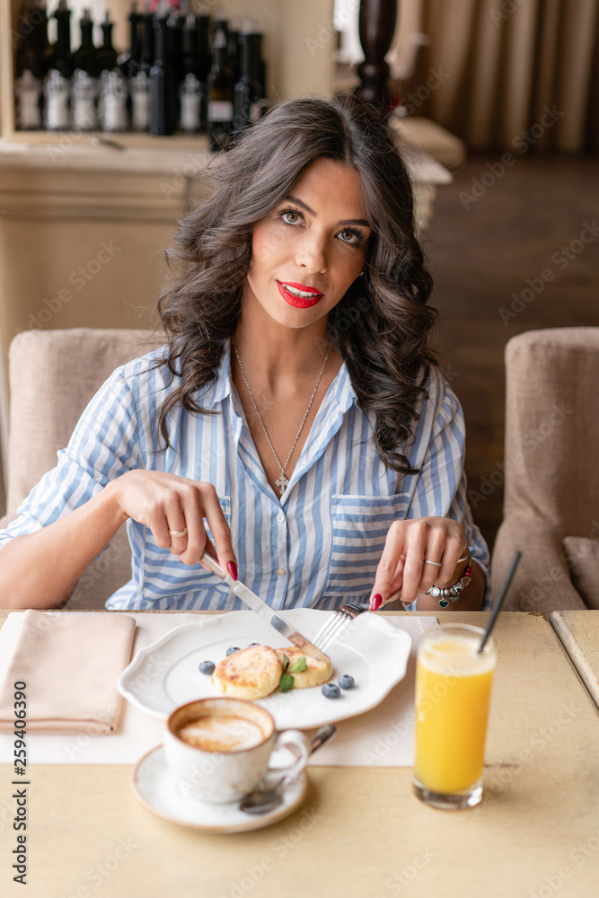 Funny and happy boy having Breakfast. Light brunch near window in a cafe. Croissants, omelet, orange juice and many different dishes on the table in the cafe.