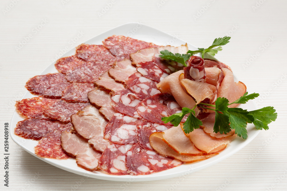 There is a variety of sausages and prosciutto on the plate, the meat assortment is decorated There is a variety of sausages and prosciutto on the plate, the meat assortment is decorated