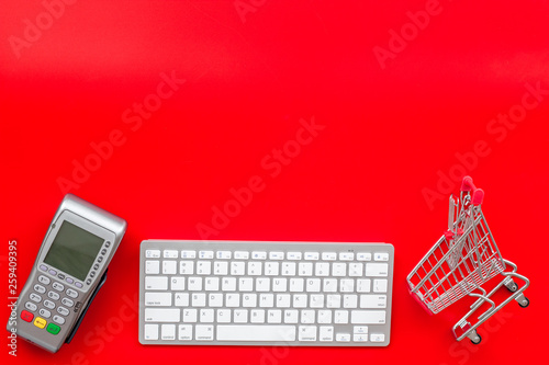 making purchase online with card machine, keyboard and mini trolley on red desk background top view