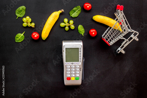 Online shopping concept with trolley, card machine near producs on black background top view photo