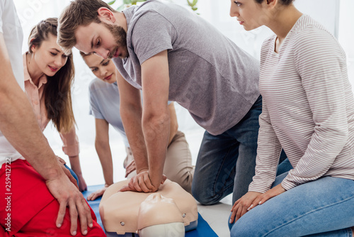 group of people looking at man performing cpr on dummy during first aid training photo