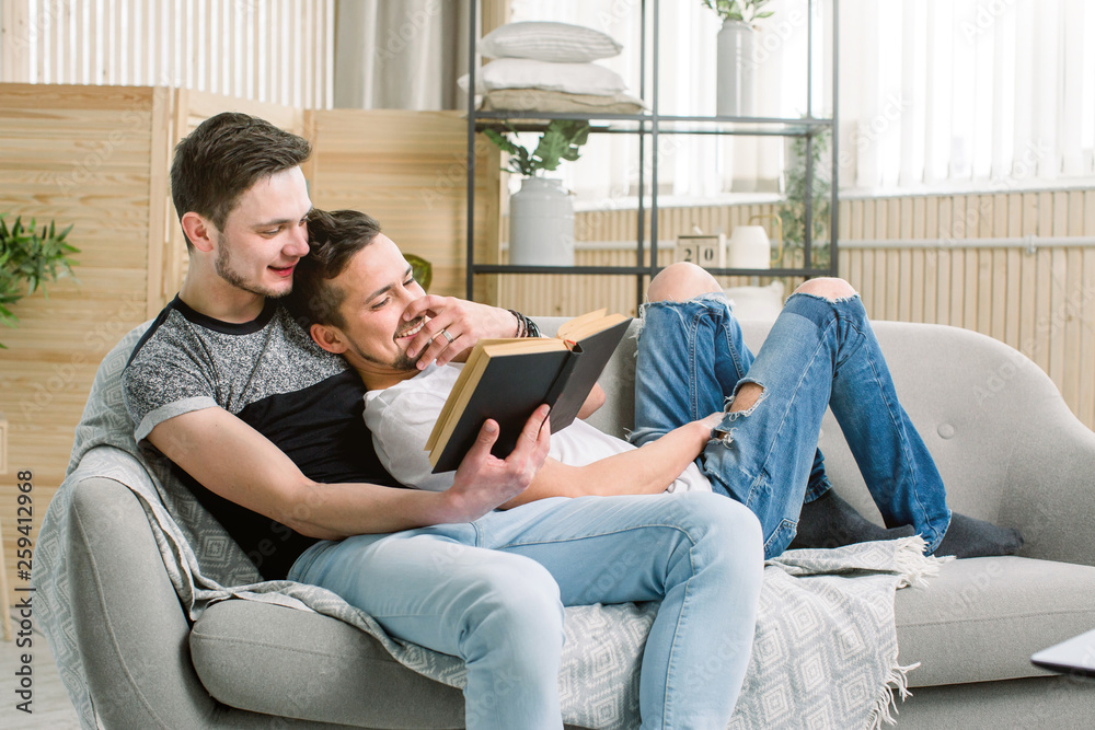 Attractive gay couple reading book on the sofa at home in living room