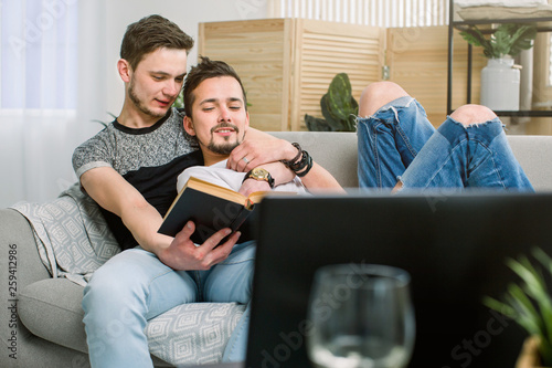 Attractive gay couple reading book on the sofa at home in living room