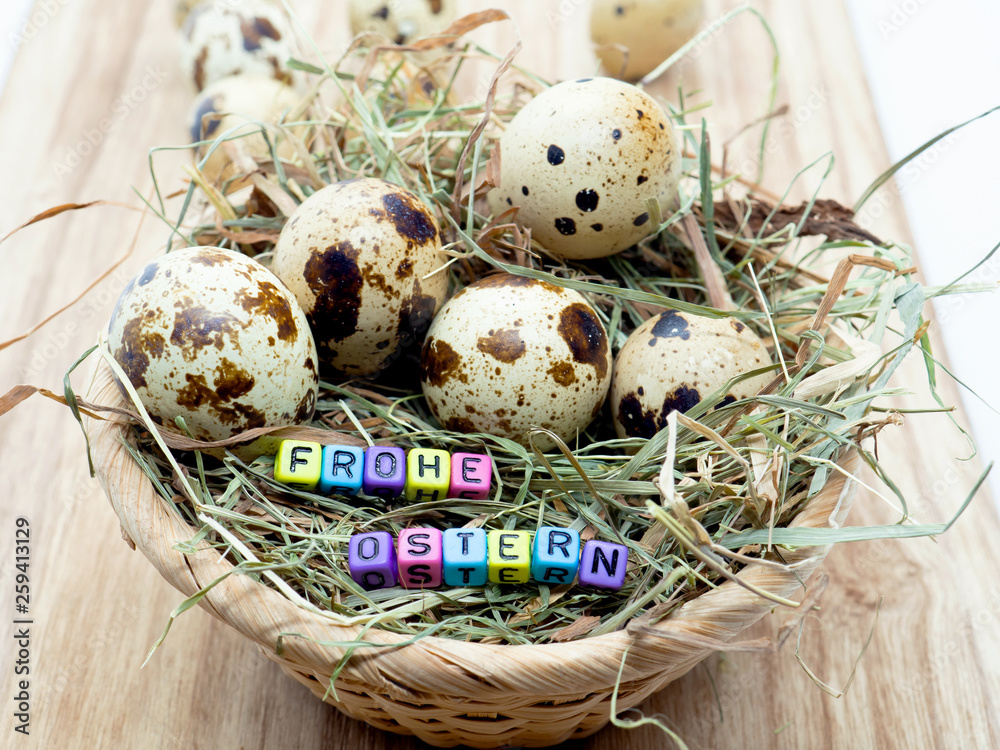 Obraz premium Wachteleier in einem kleinen Korb (Osternest) mit Text Frohe Ostern