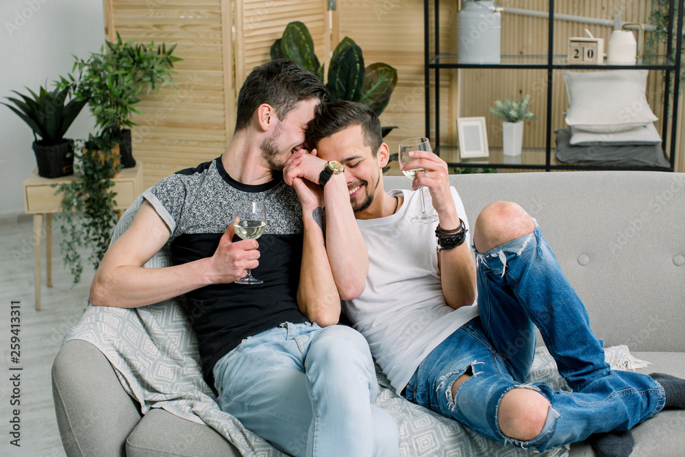 Fotka „Young gay men holding hands on sofa at home. Shy gay couple showing  love and romance, drinking wine“ ze služby Stock | Adobe Stock