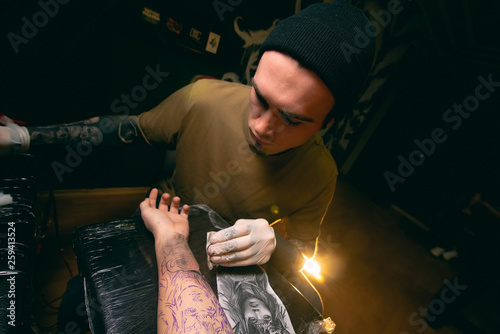 Professional tattoo artist makes a tattoo on the client's hand close-up. Hands in white gloves written out the body of a girl art print