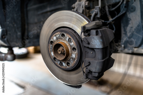 Front brake discs with caliper and brake pads in the car, on a car lift in a workshop.